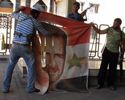 Free Syrian Army members tear a banner with picture of Syria's President Al Assad at Syrian border crossing building between Syria and Turkey at Jarablus