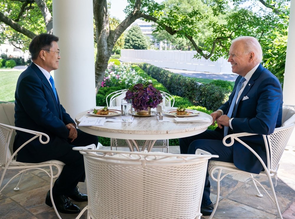 President Moon Jae-in sits opposite of President Joe Biden at an outdoor table.