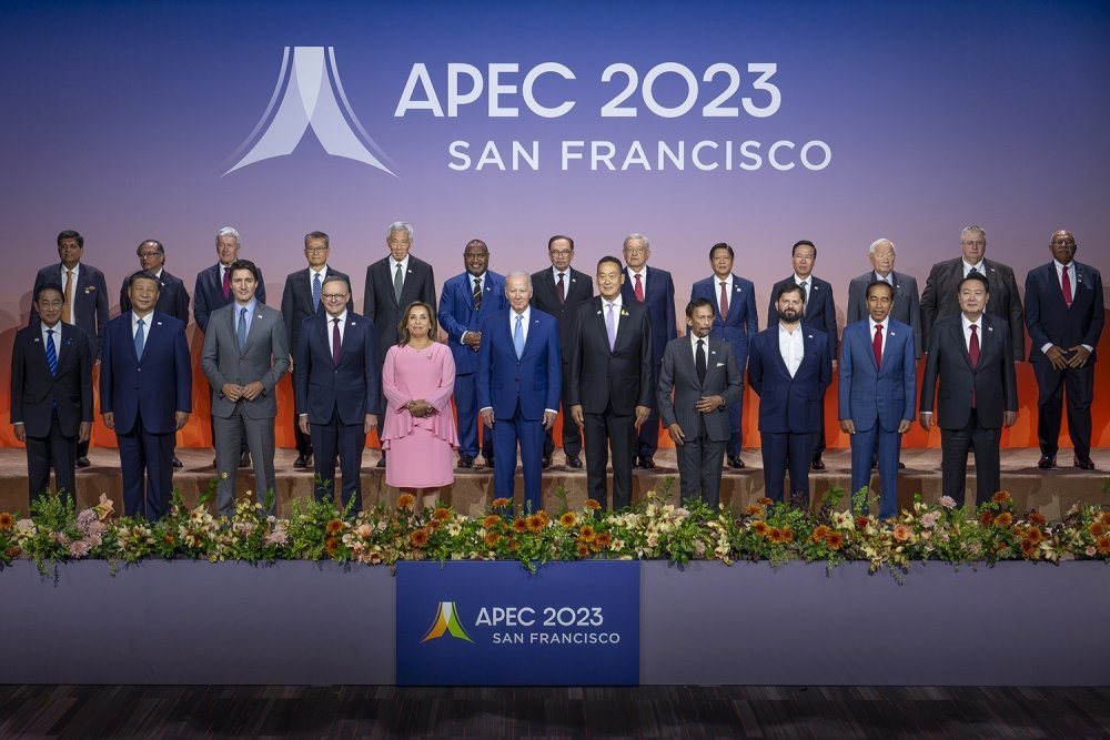 A large group of world leaders stand on a stage in front of a logo for APEC 2023.