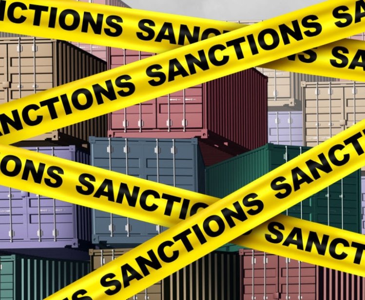 An image of cargo containers with yellow tape that says sanctions over top of them.