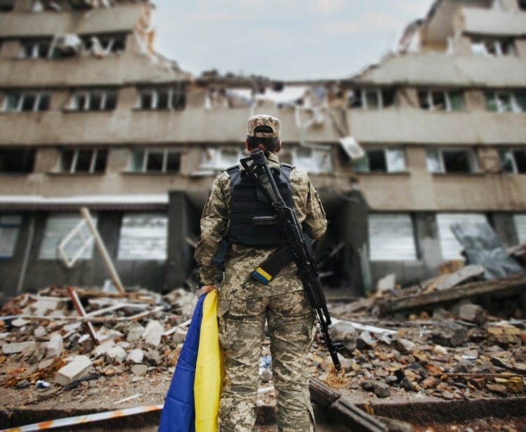 Ukrainian military woman with the Ukrainian flag in her hands on the background of an exploded house. 