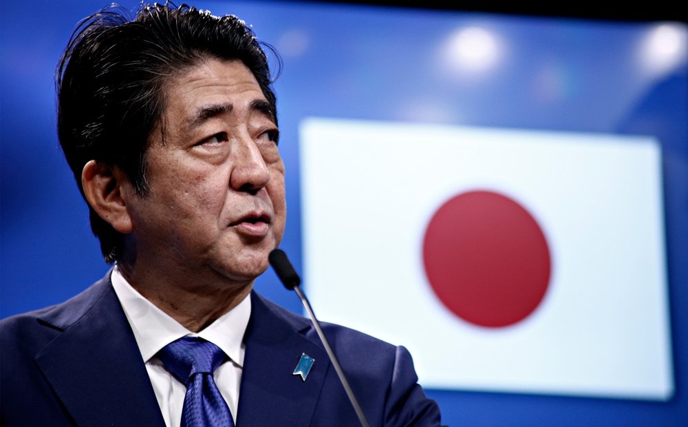 Prime Minister Shinzo Abe speaks in front of a Japanese flag at an event.