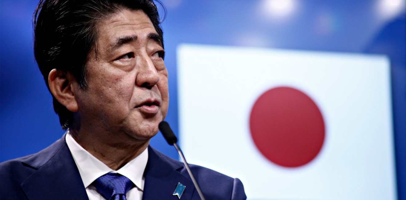 Prime Minister Shinzo Abe speaks in front of a Japanese flag at an event.