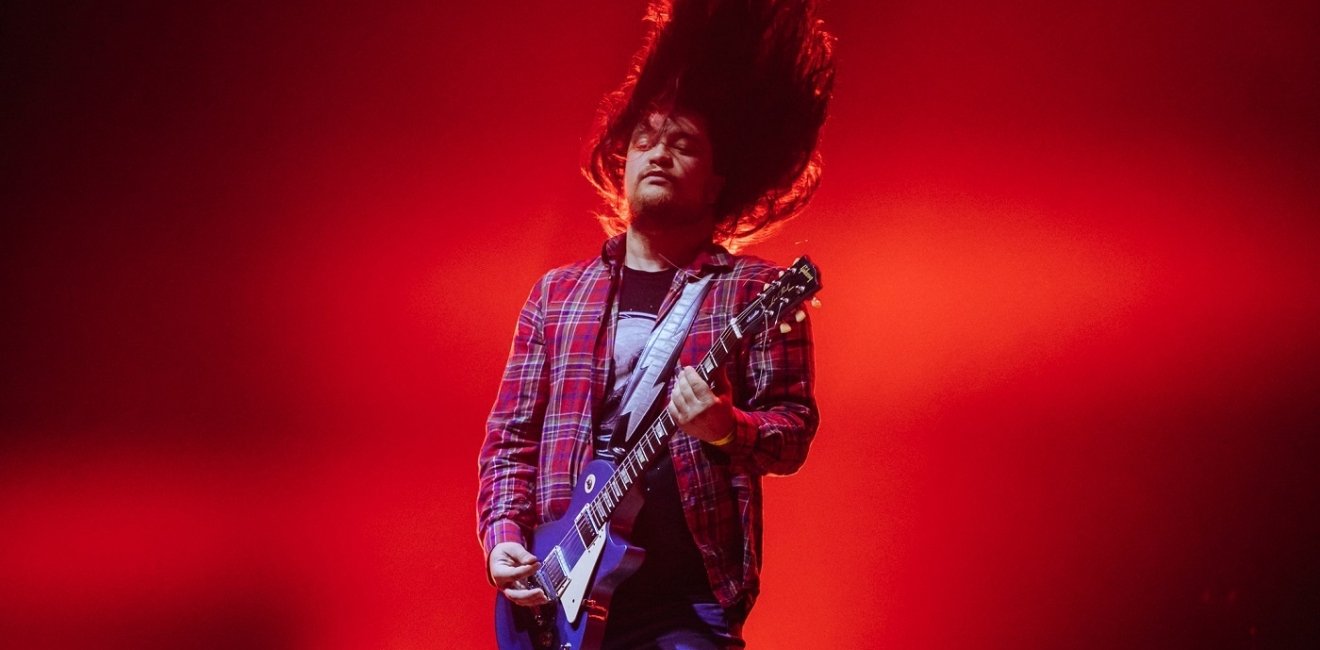 Man on stage whipping hair and playing the guitar