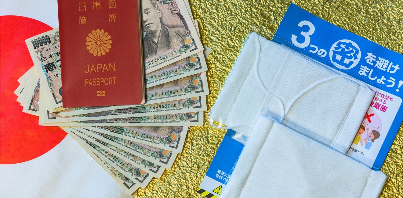 Cloth masks, a leaflet, and 100,000 yen cash sitting on a background with a Japanese flag.