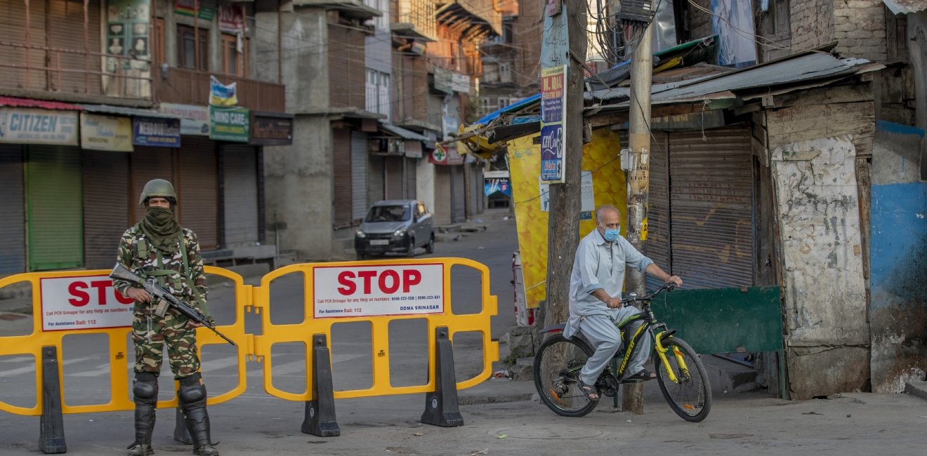 A Kasmiri man on a bicycle rides past a barricade guarded by a soldier.