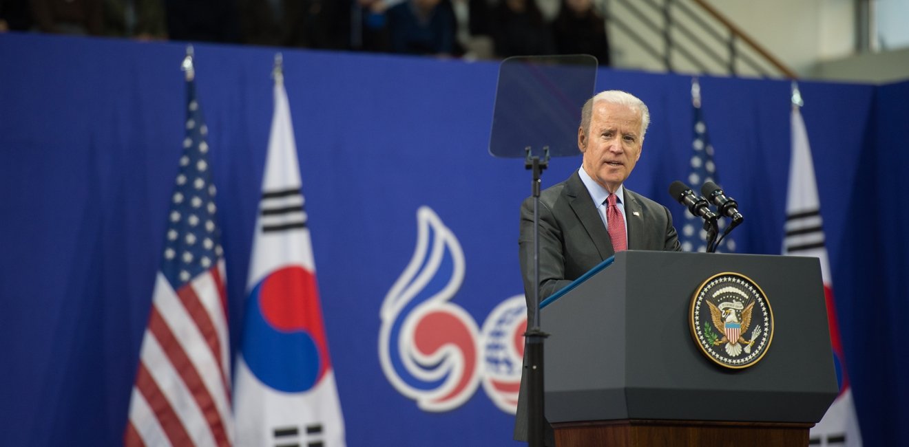 Joe Biden stands at a podium delivering a speech in front of U.S. and South Korean flags