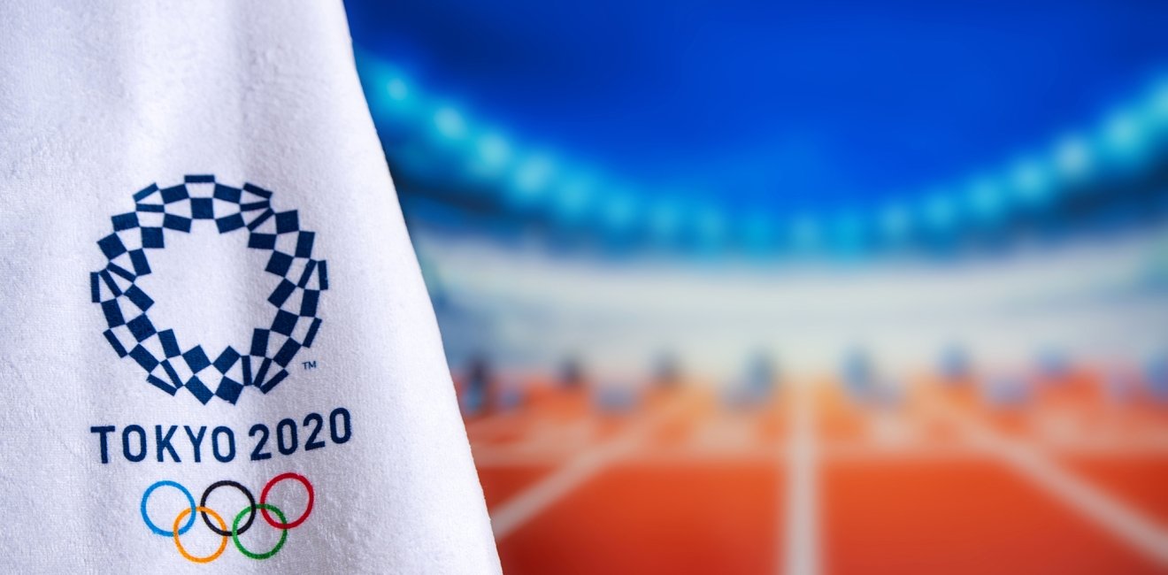 A towel with the logo for the Tokyo 2020 olympics in the foreground with track and field starting blocks in the background in soft focus