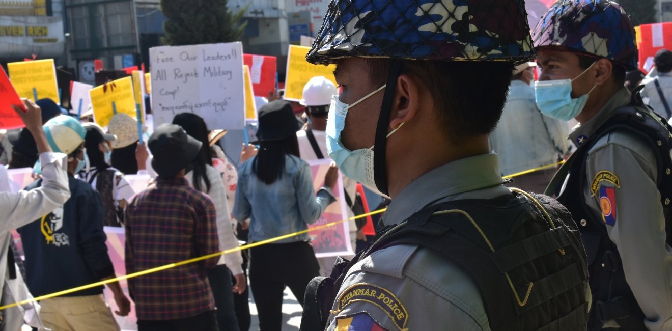 Two soldiers in miliary uniform watch a crowd of protestors.