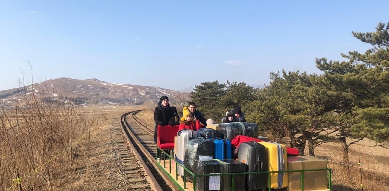 A group of people hand pushing a small railway cart loaded with lugagge.