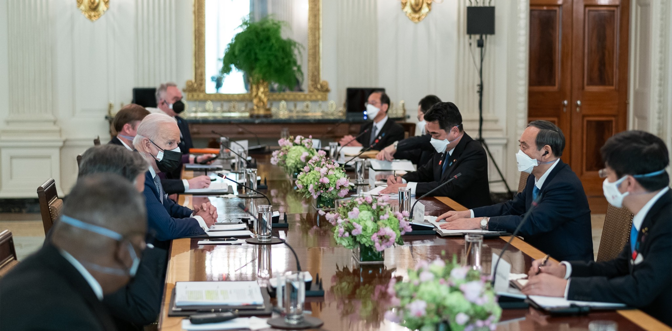 A group of men including President Biden and PM Suga sit around a conference table