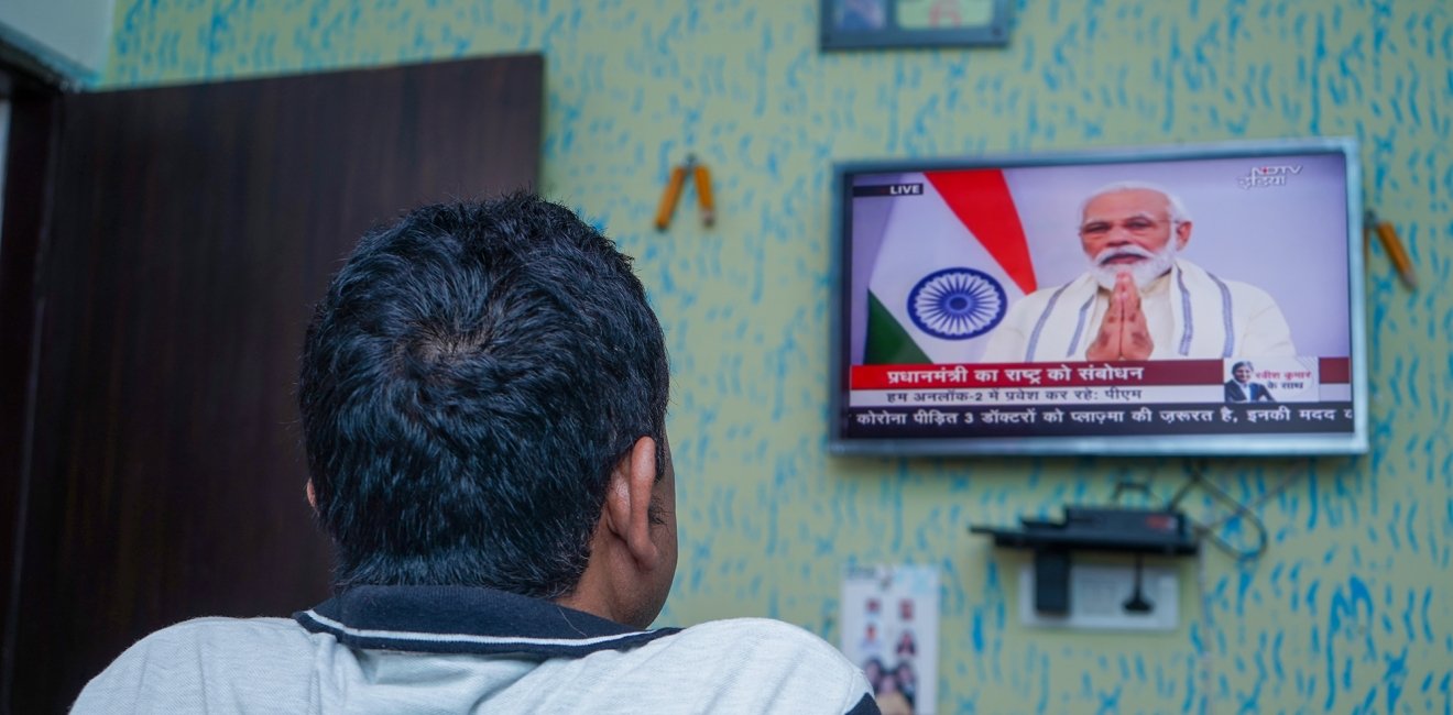 A man watches a television that is playing an announcement from PM Modi.