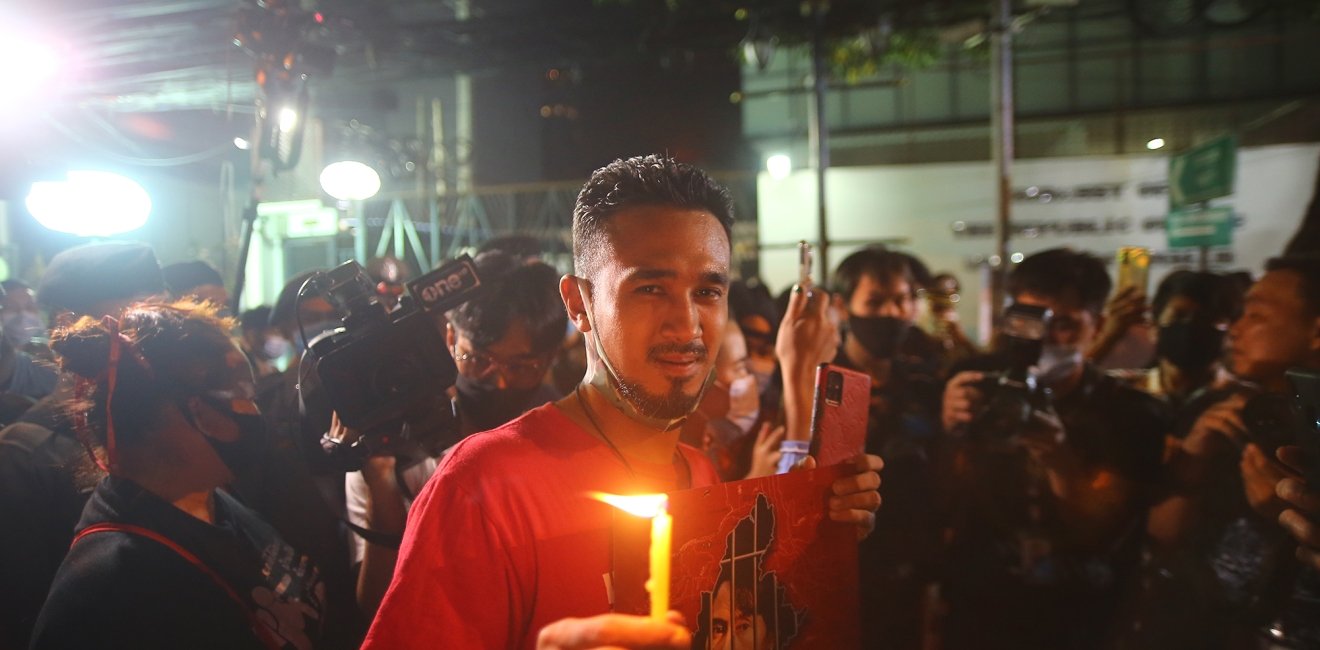 A man stands in a crowd of protestors holding a lit candle at night.