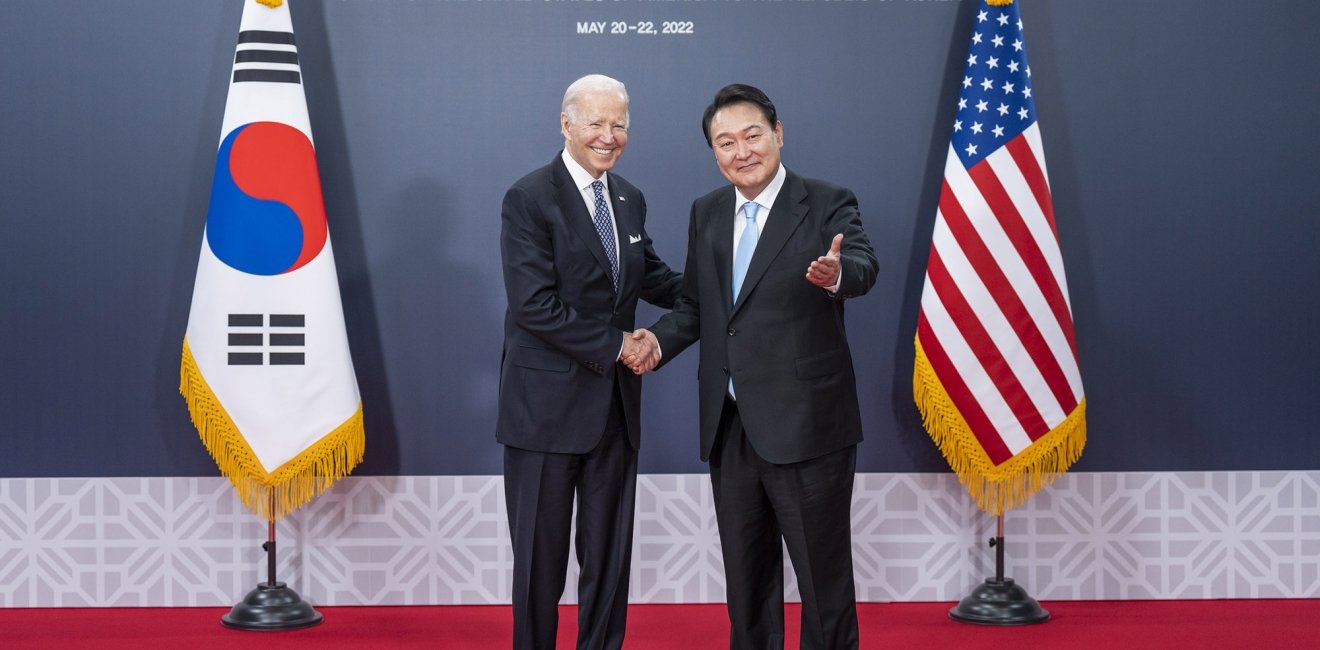 President Biden and President Yoon shaking hands in front of a banner announcing the official visit in 2022.