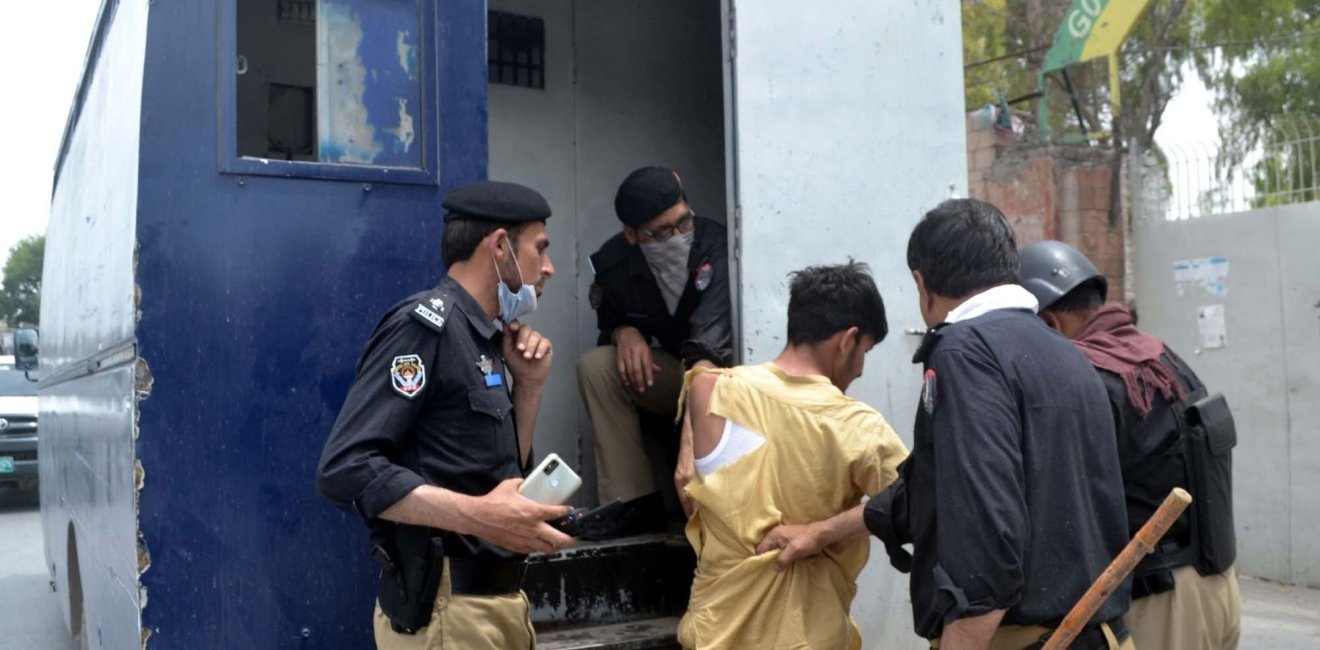 Police officials are pushing a man with torn clothing into the back of a police vehicle after he has been arrested.