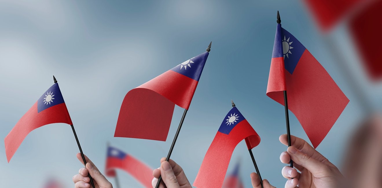 A close up of hands waving small Taiwanese flags.