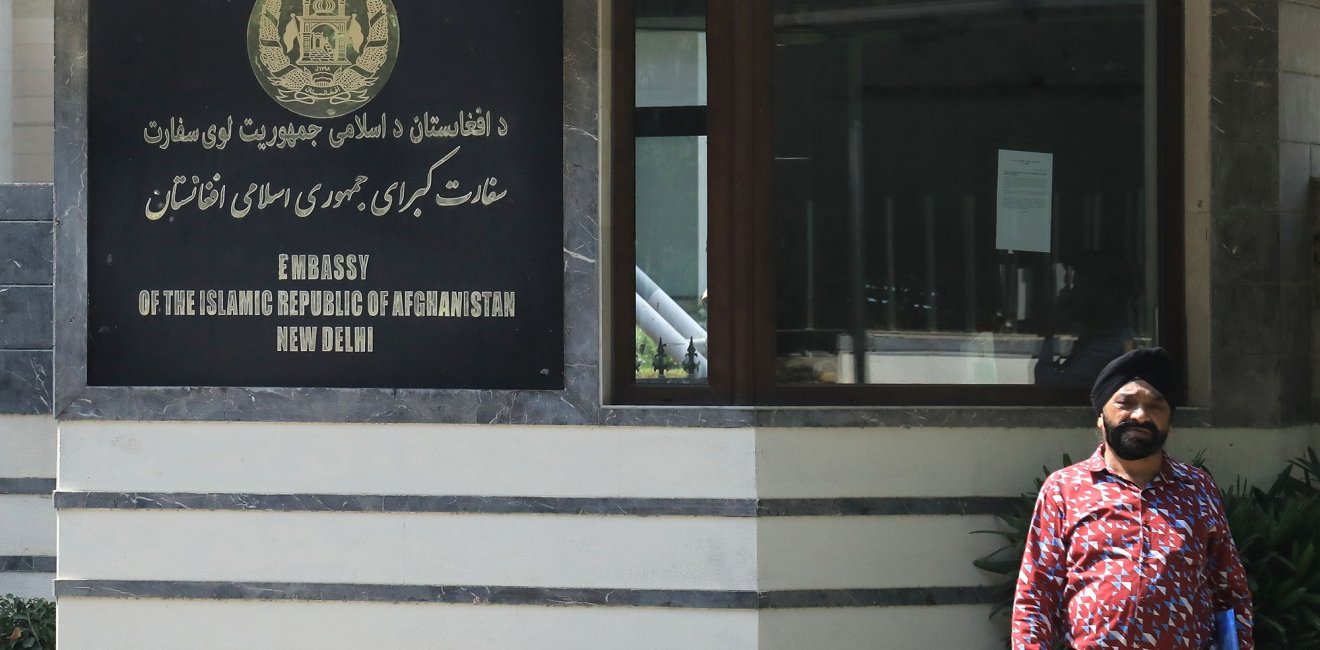 A man stands outside a building with a sign that reads Embassy of the Isalamic Republic of Afghanistan, New Delhi