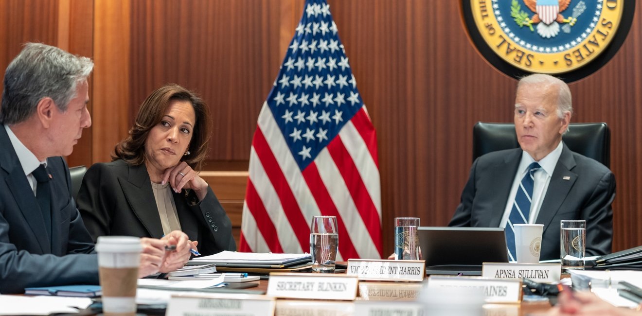 Secretary Blinken, Vice President Harris, and President Biden sit at a table while having a discussion.