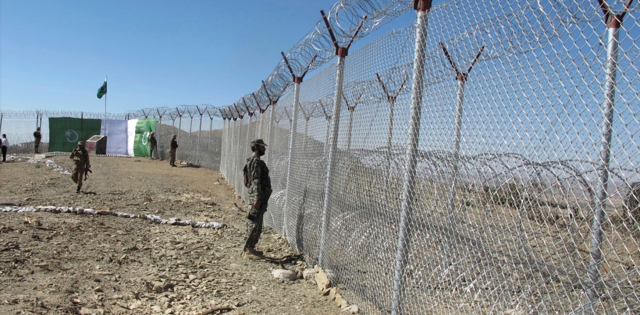 A uniformed soldier stands at a wire border fence.