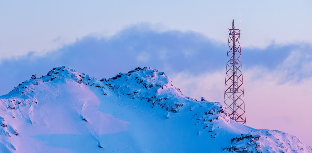 Telecommunication tower on the slope of a snowy mountain. Winter arctic landscape. View of the mountain top and the metal tower with antennas. Communication in the far north in the polar region.