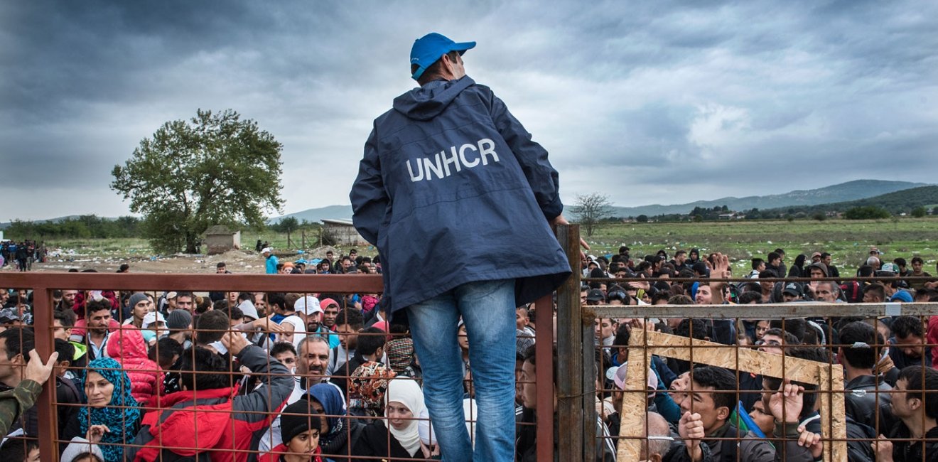 Gevjelija, Macedonia - September 26, 2015. A UNHCR employee talks to refugees as they wait during a rainstorm to enter inside a refugee camp near the town of Gevgelija at the Macedonian - Greek border