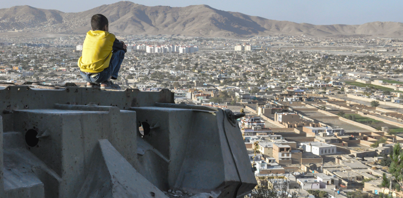 KABUL, AFGHANISTAN 2012: Boy sitting on Destroyed Tank on the hills over Kabul City in Afghanistan