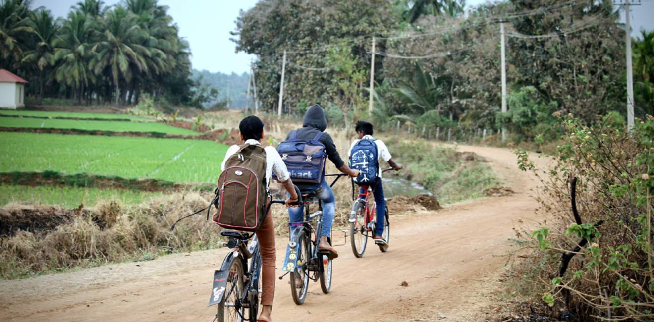 South Indian village children(friends) are going to school by bicycles(cycles or bikes) on a mud road in a nearby village