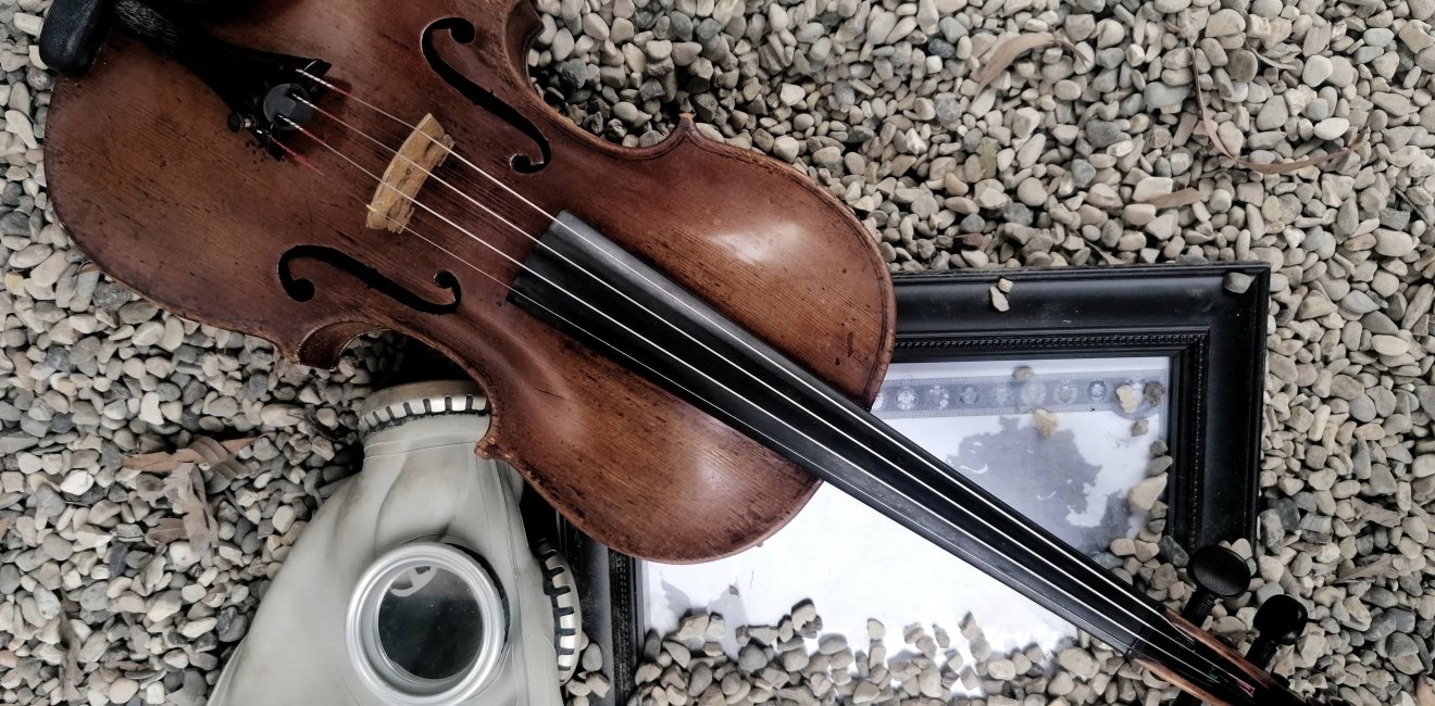 Image of a gas mask, violin and framed photo in gravel