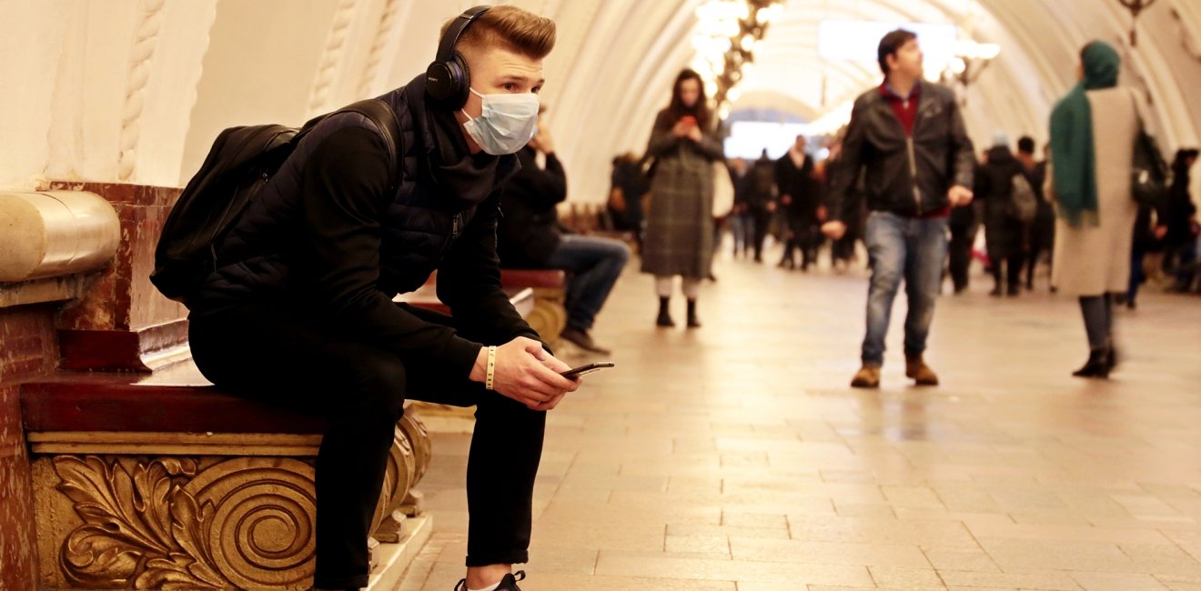 A young man with a backpack sits at a Moscow metro station with a medical mask