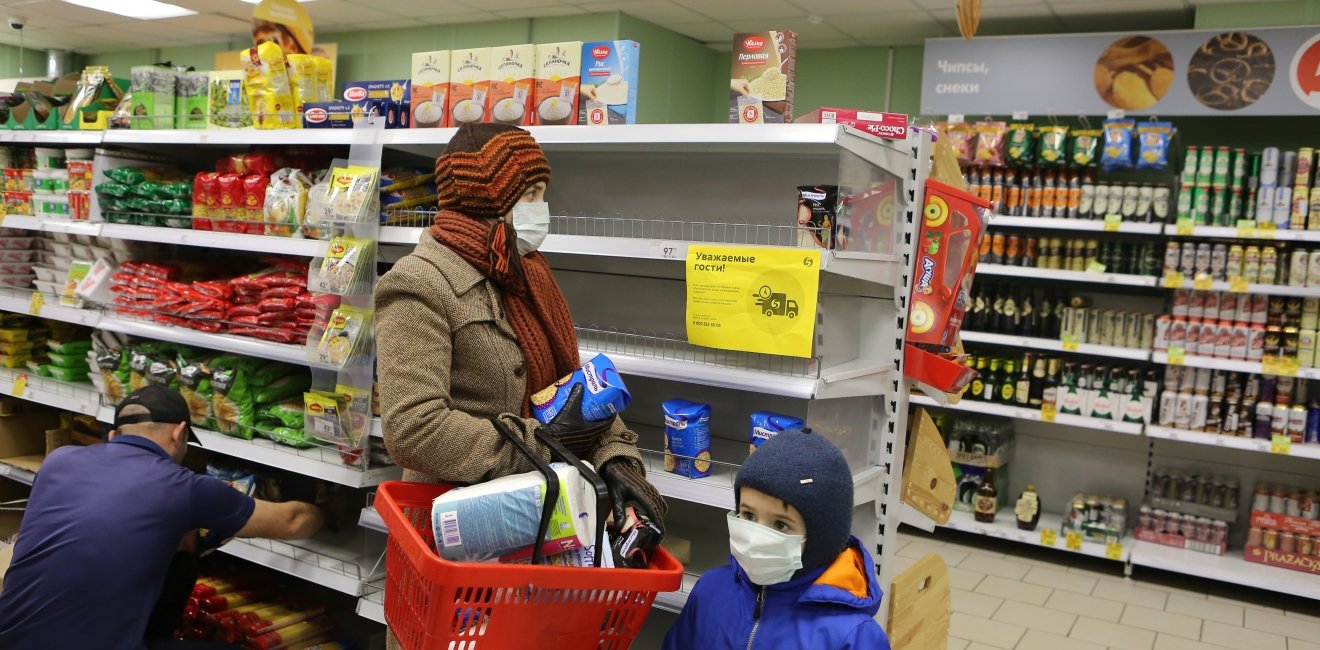 Shoppers in a Moscow grocery store where there are few products on shelves, holding buckwheat and toilet paper. 