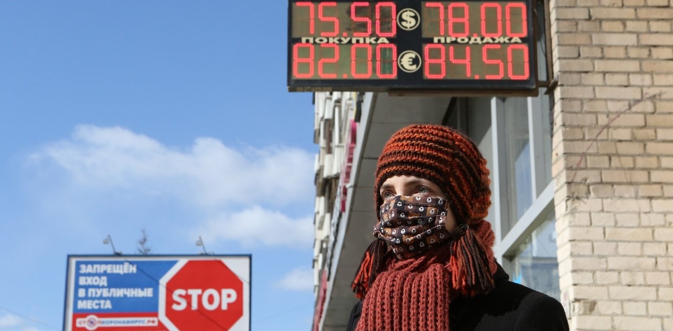 A woman stands in front of a sign displaying the ruble's exchange rate