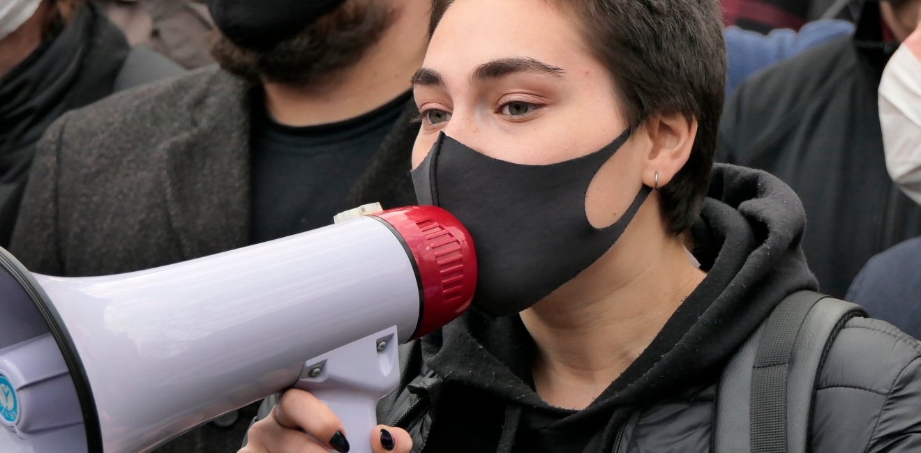 Kiev/Ukraine - October 26, 2020: young dark haired woman with medical mask on face shout out slogans to loudspeaker at street protest rally against abortion ban in Poland near Polish embassy in Kyiv