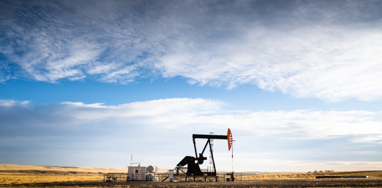 An industrial oil pump jack working on farm land under a morning sky 