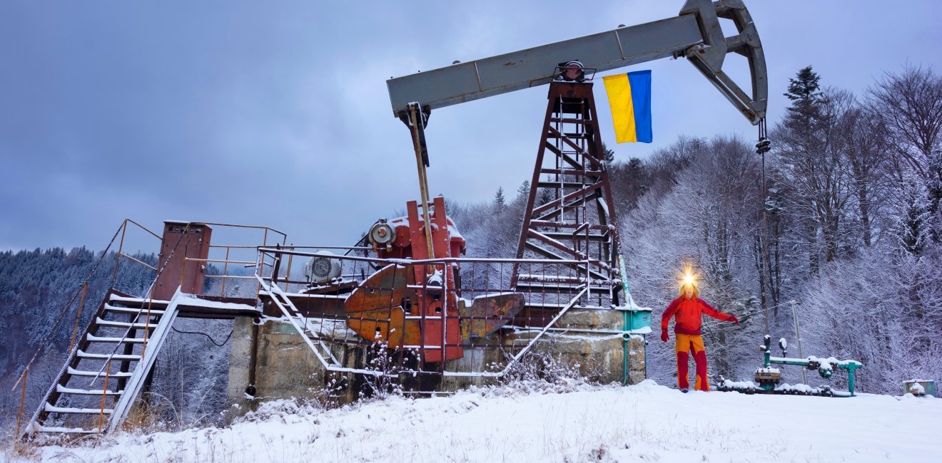 A working engineer at an oil and gas development of an old field checks the operation of mechanisms and control systems in the mountains after a winter in early spring. Flag of Ukraine yellow-blue.