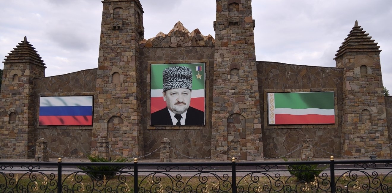 Portrait of Akhmad Kadyrov on a old stone building next to Russian and Chechen Flags