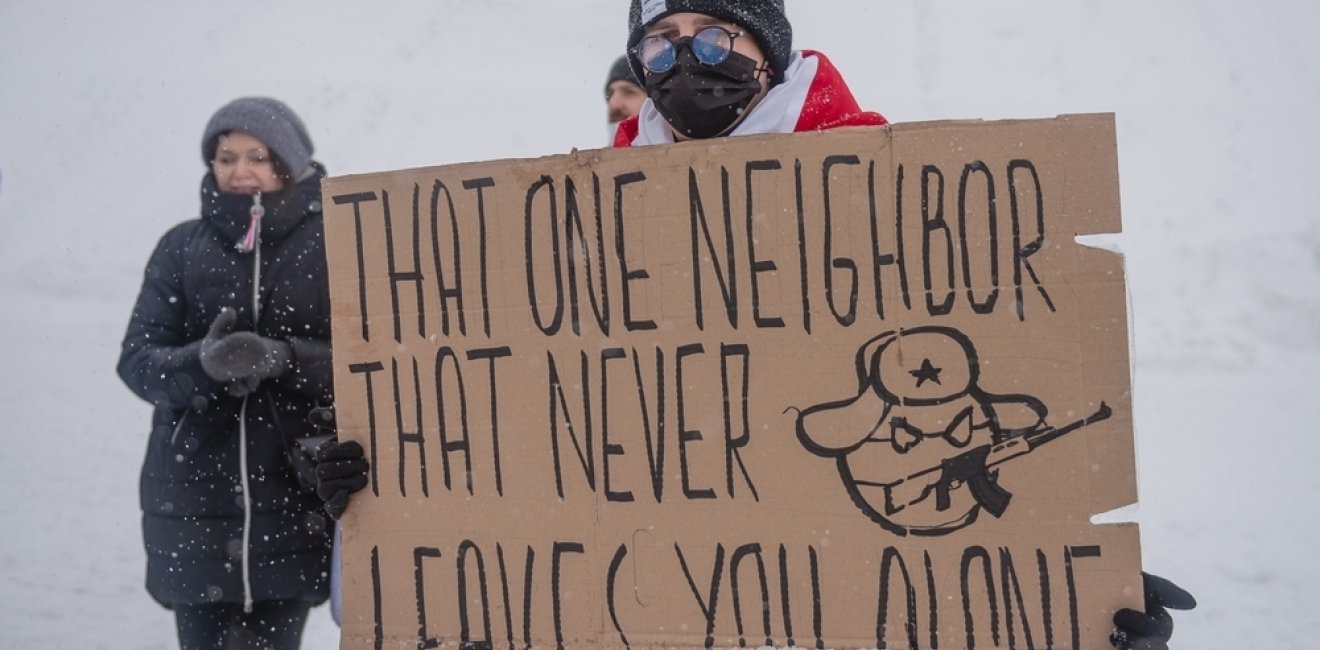 Protester in snow with sign that reads "That one neighbor that never leaves you alone" and a caricature representing the Russian state