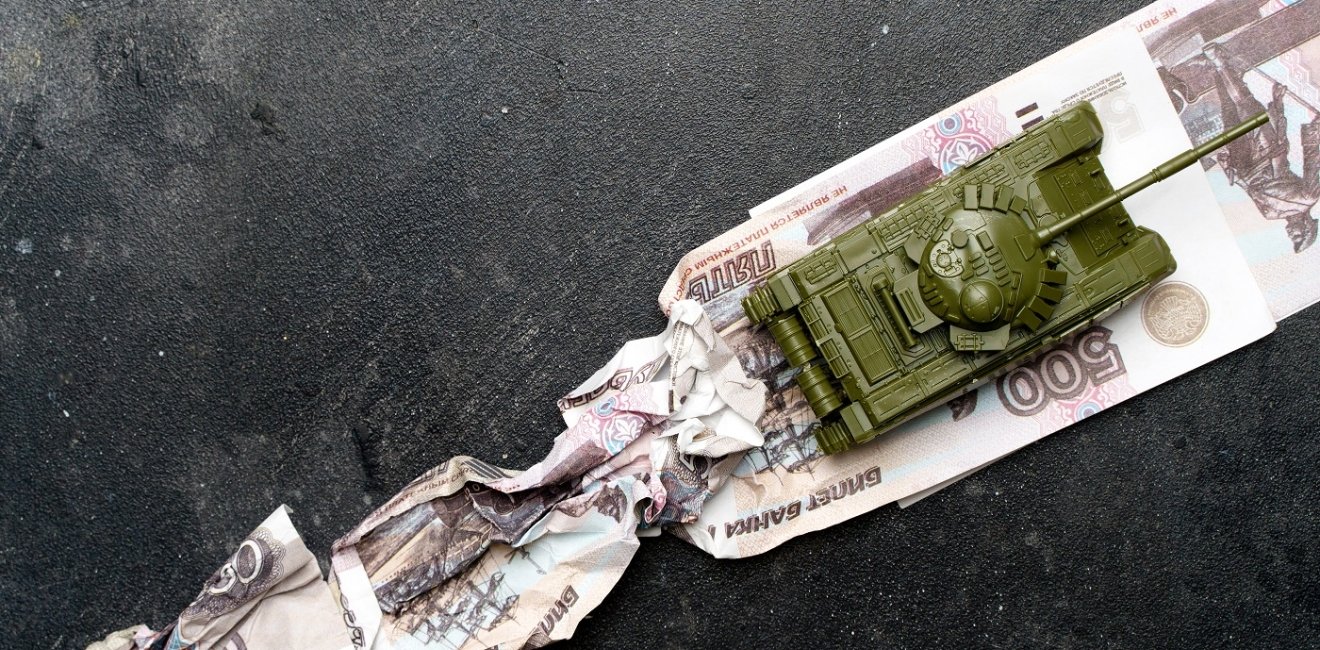 A toy tank runs over Russian ruble notes