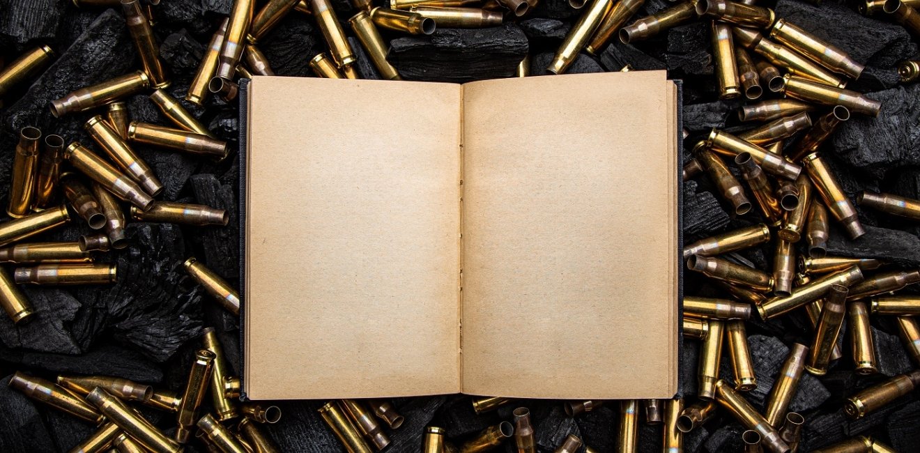 open book in a black hardcover with yellowed blank pages. Empty gun cases lying on charred coals.