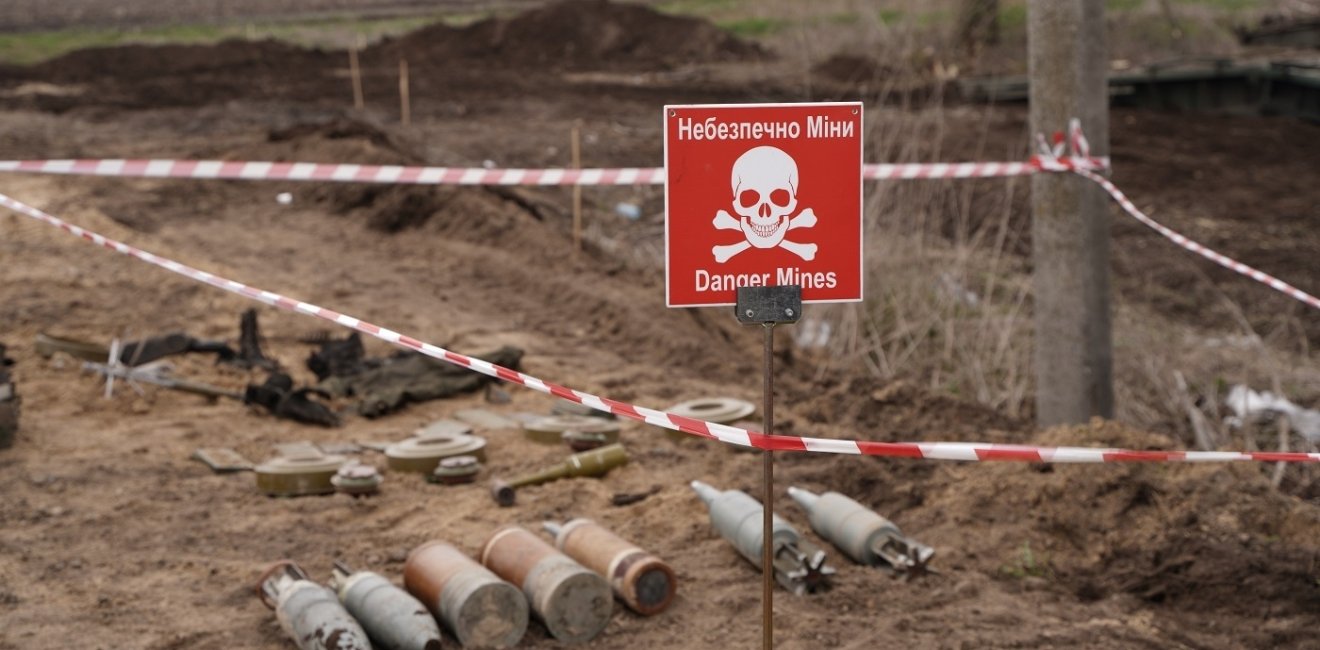 Unexploded ordinance lying in a field next to a red warning sign