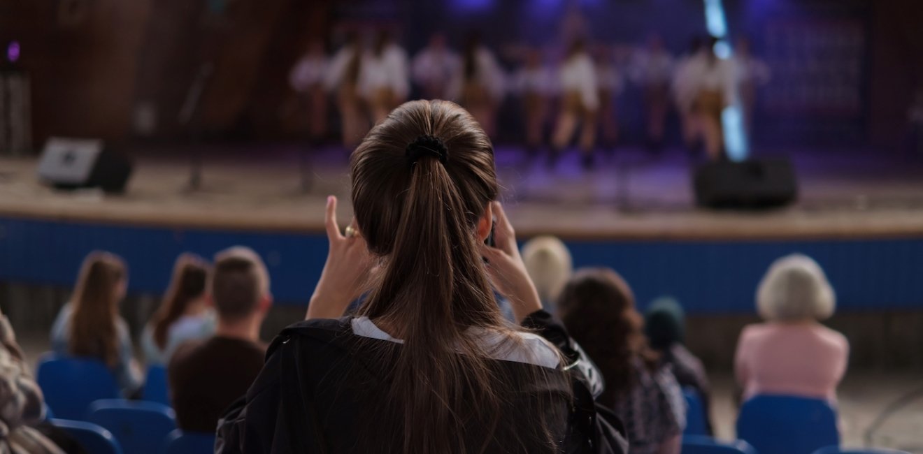 Girl taking a photo of dancers on the stage. 