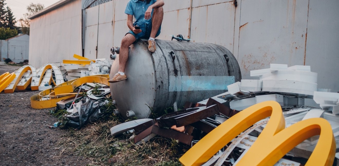  Young man sitting on VR headset and McDonalds logo "M" on dirty rubbish heap dump trash litter garbage.