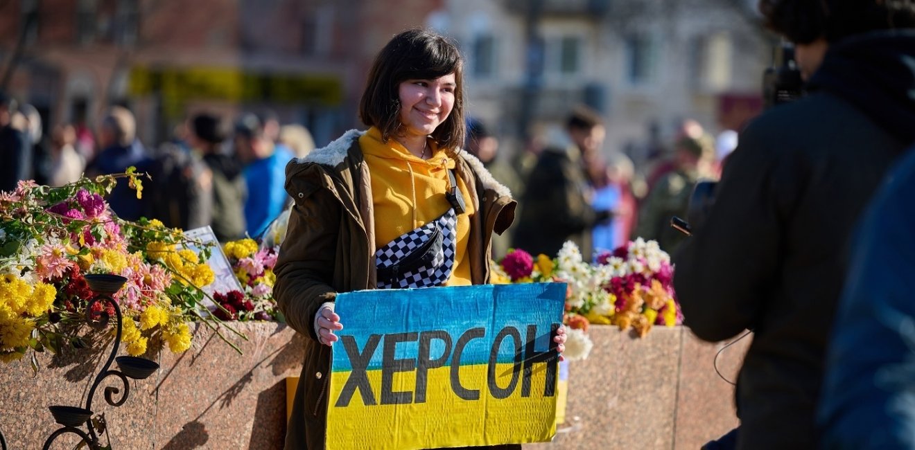 Woman holding sign with colors of Ukrainian flag and "Kherson" written in Cyrillic 