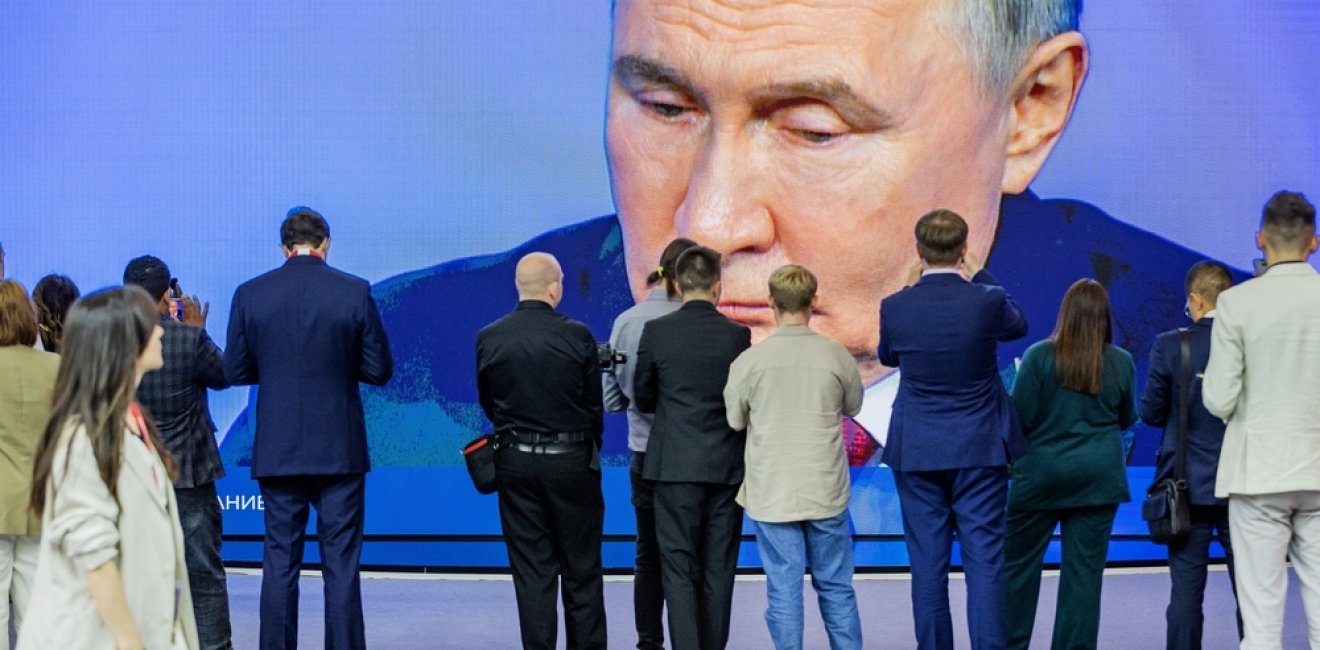 A crowd of people take pictures and watch a largescreen broadcast of President Vladimir Putin. 