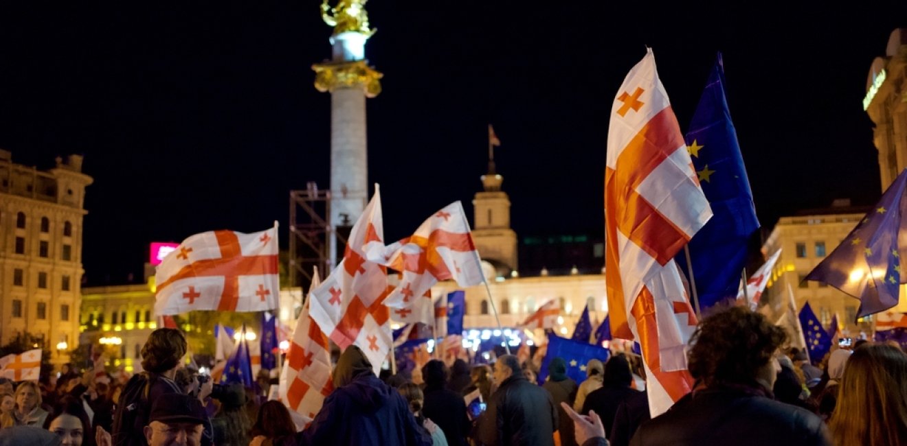 A crowd of protesters in front of the monument in Liberty Square in Tbilisi wave Georgian flags and EU flags. 