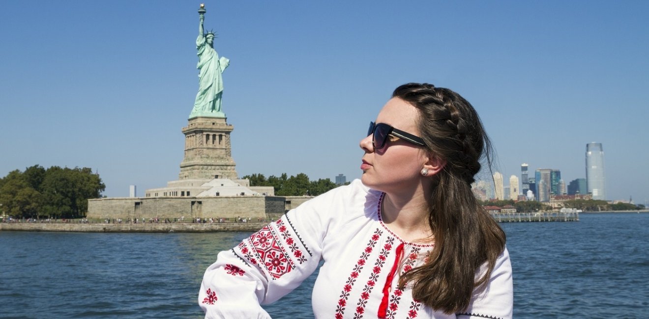 Woman in traditional Ukrainian dress sitting in front of the statue of Liberty