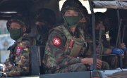 Soldiers in uniforms and masks sitting on a truck.