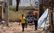 Young people walk along a street marked by destruction. A bloody power struggle has been raging in Sudan for more than 16 months, triggering a refugee crisis. Mudathir Hameed/picture-alliance/dpa/AP Images.