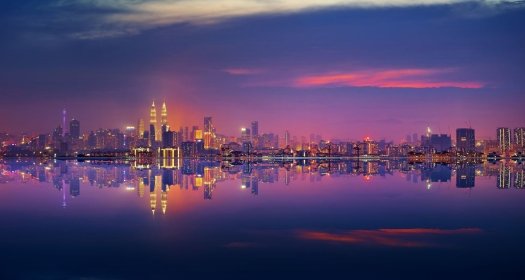 A panoramic shot of the city of Kuala Lumpur at night, seen from the water.