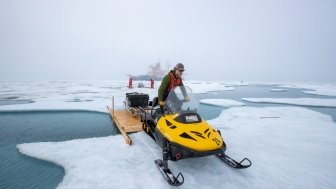 Matthew Shupe drives a snowmobile over a bridge toward a measurement site on Jul 29, 2020, photo courtesy of Alfred-Wegener-Institut/Lianna Nixon (CC-BY 4.0). 