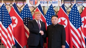 Donald J. Trump stands next to Kim Jong Un as they shake hands and pose in front of U.S. and North Korean flags